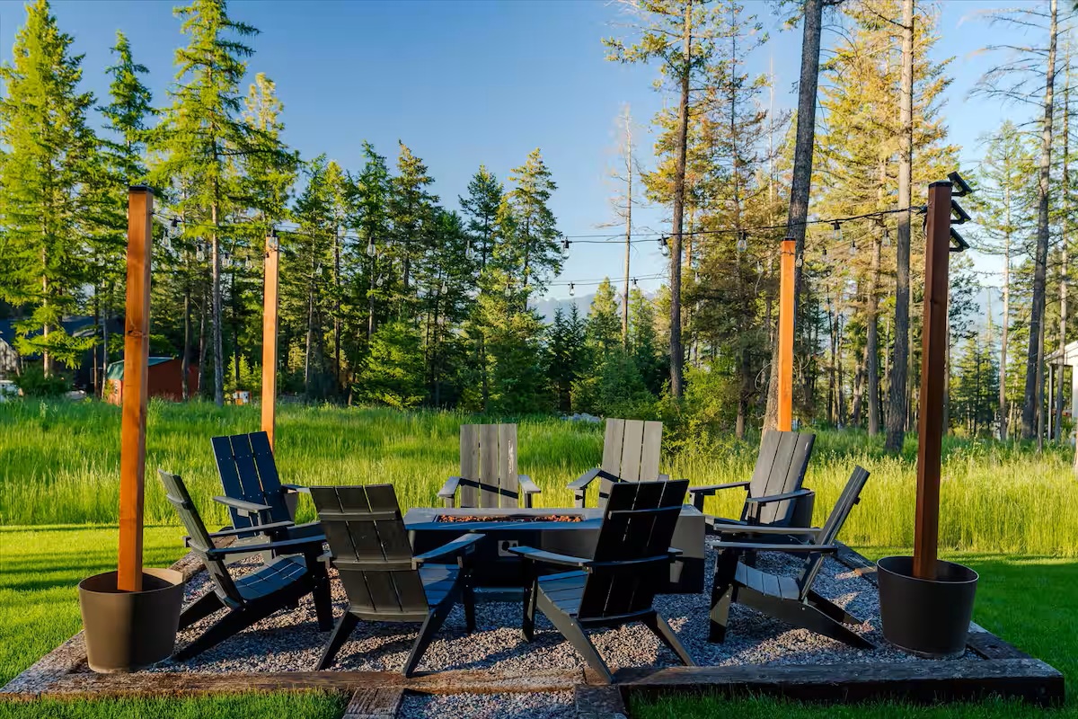 Fire pit ringed with Adirondack chairs under string lights and tall pines