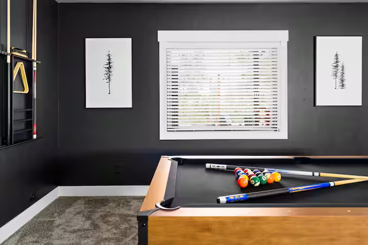 Pool table racked and ready beneath framed pine prints in the charcoal game room