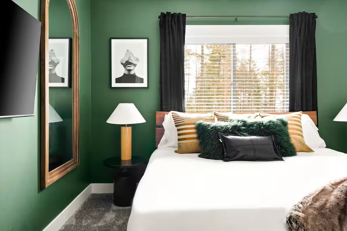 Green bedroom with queen bed, mirror and forest window views