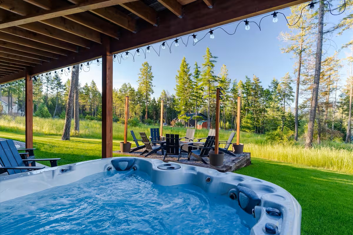 Covered deck hot tub with string lights overlooking the fire pit and pines