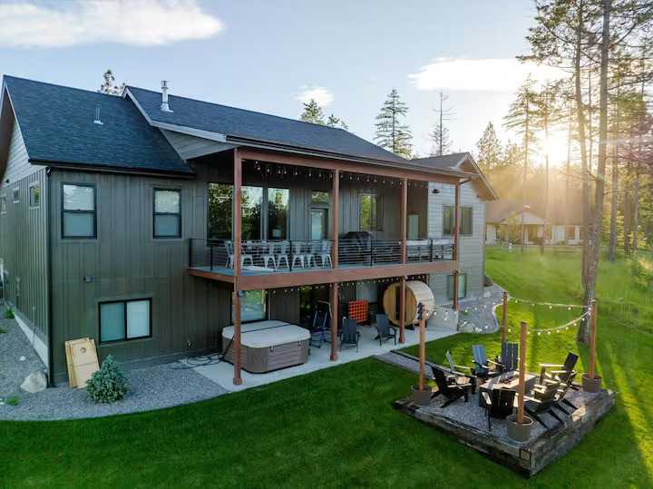 Back of the home at golden hour with a two-level covered deck, hot tub, barrel sauna and fire pit