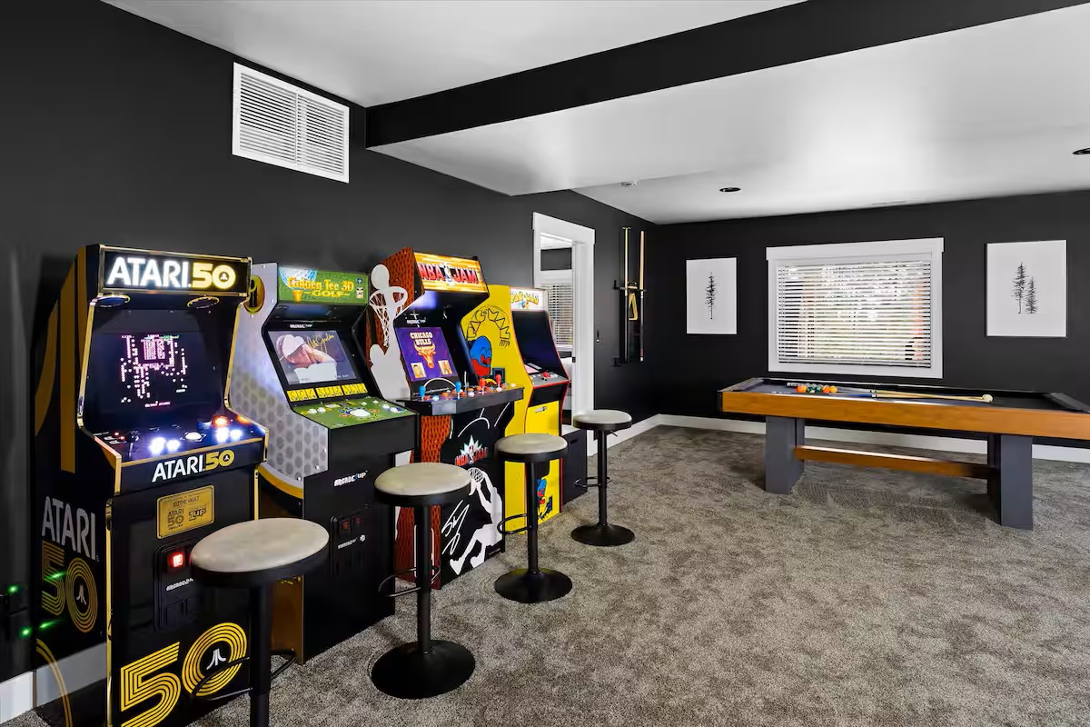 Game room with retro arcade cabinets, bar stools and a pool table