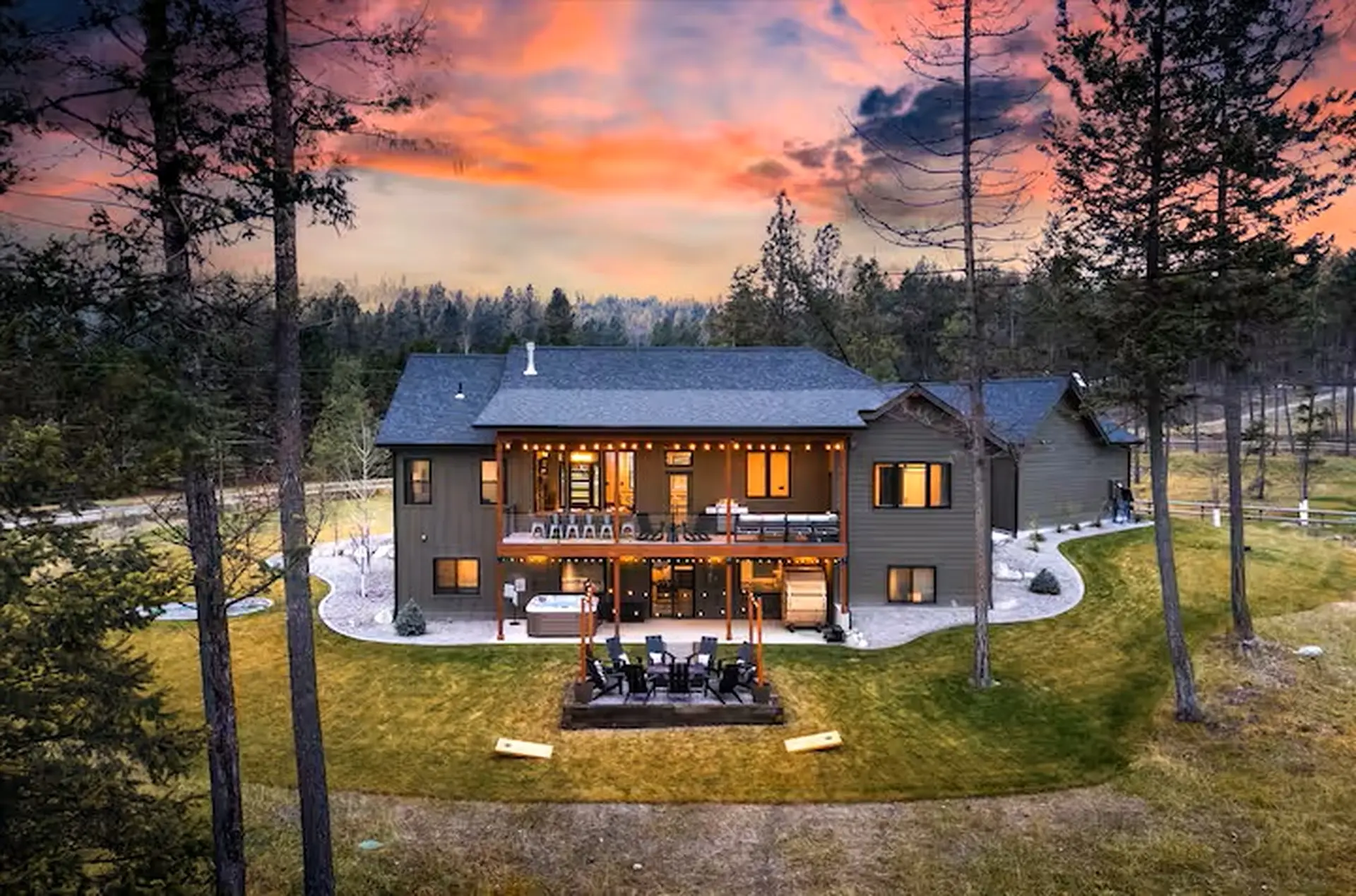 Back of the home at sunset with covered deck, string lights, hot tub and fire pit